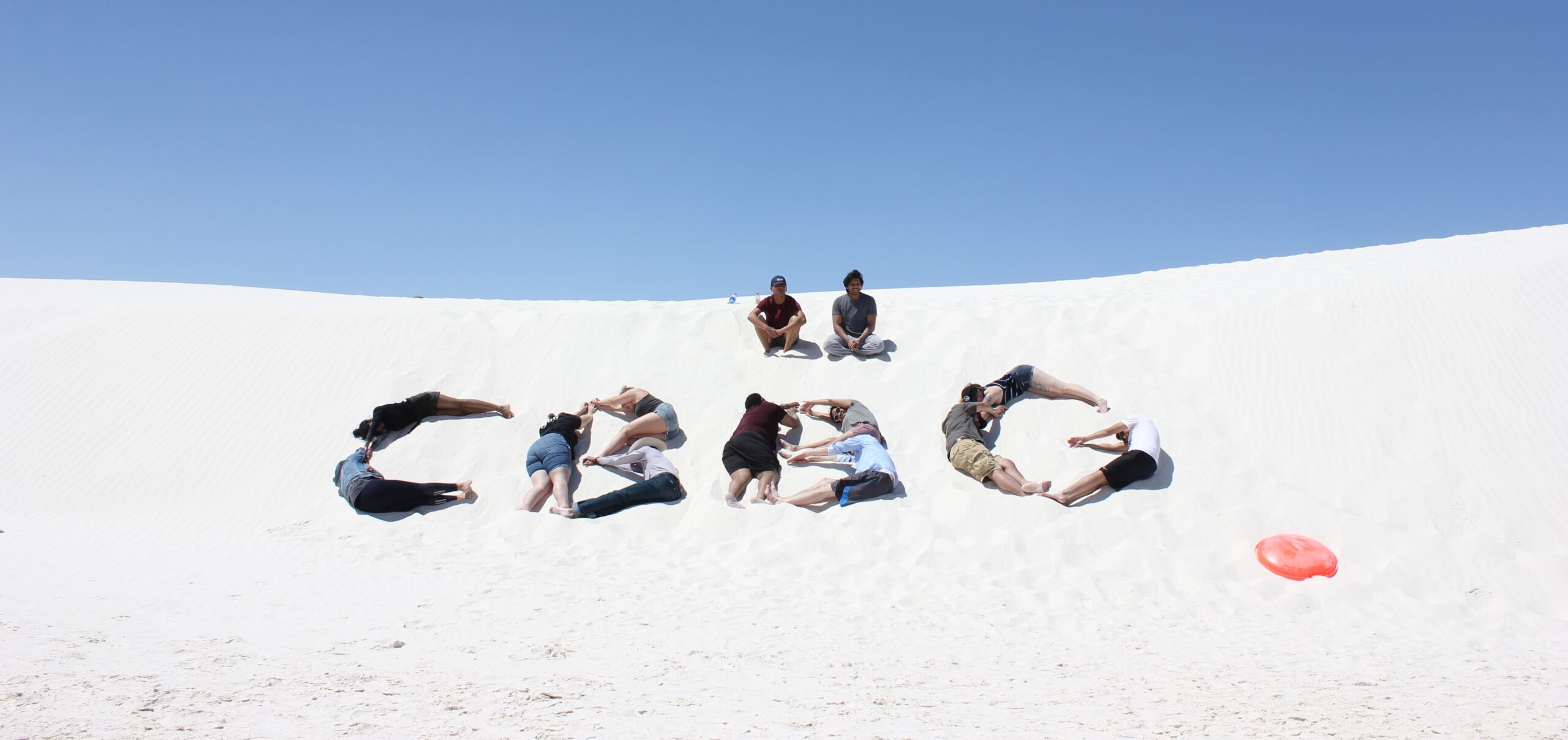 Students laying in a sand dune spelling CBBG with their bodies.